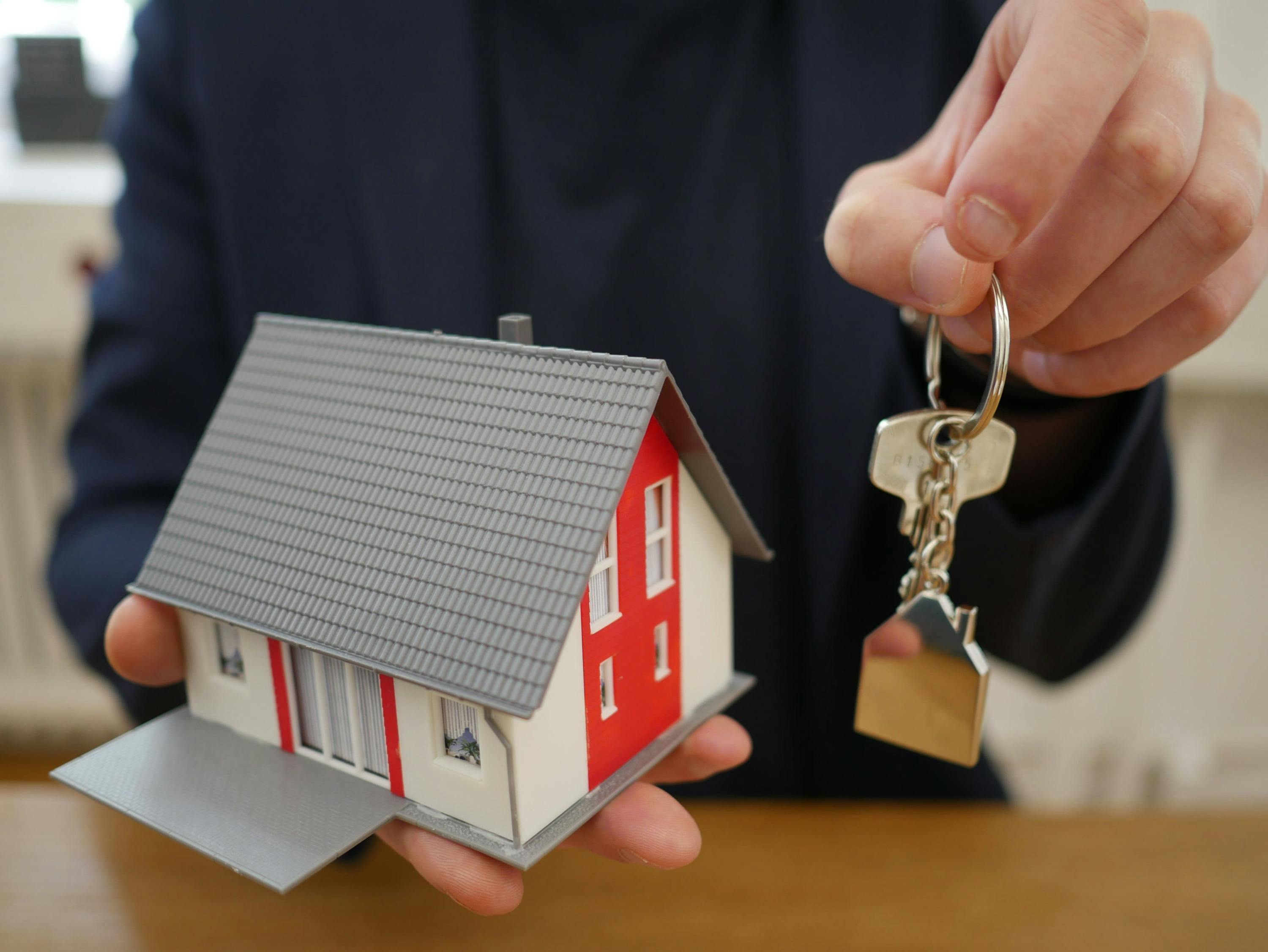 Eine Person hält ein Miniatur Haus in der einen und ein Schlüssel in der anderen Hand