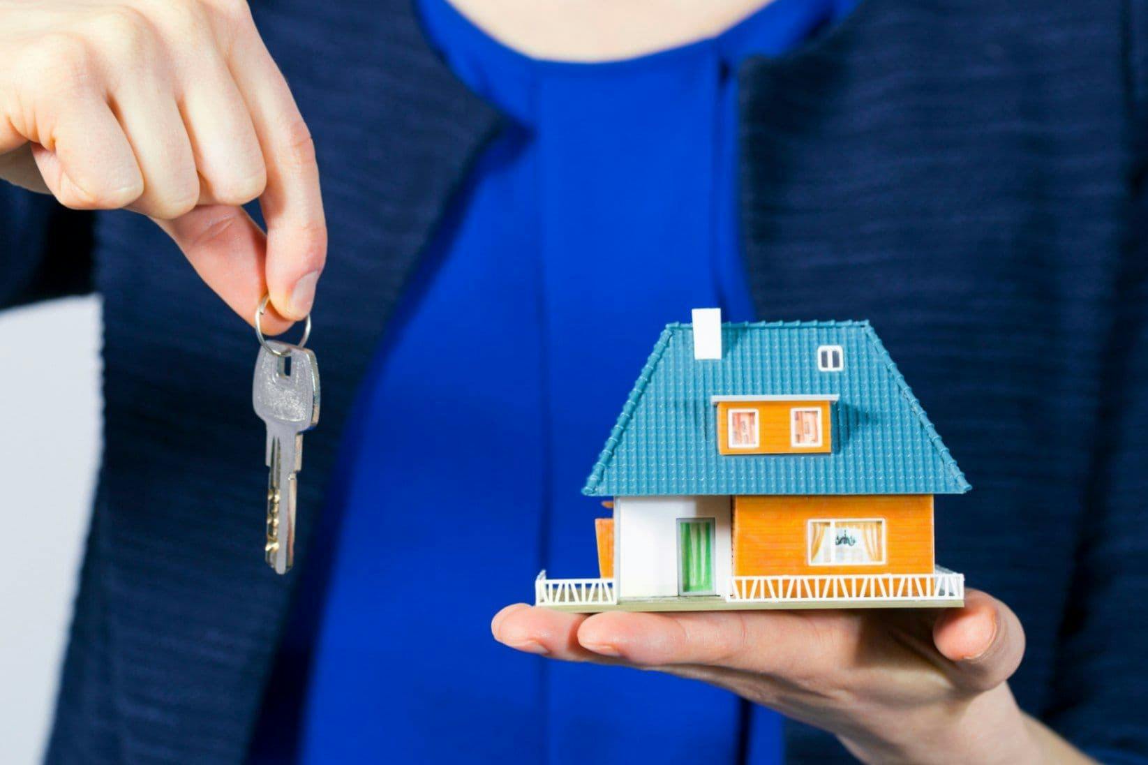 Eine Person hält in einer Hand einen Schlüssel und in der anderen Hand ein Modell Haus